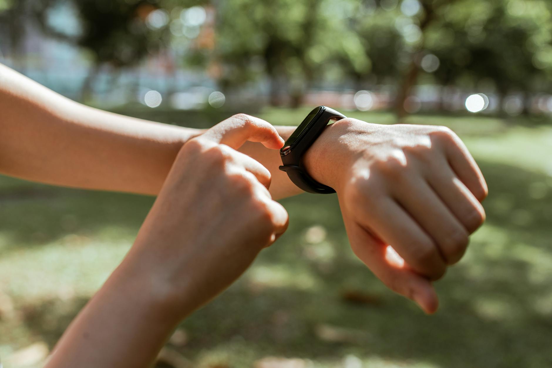Crop faceless slim female tapping on fitness bracelet screen while training time in sunny summer park