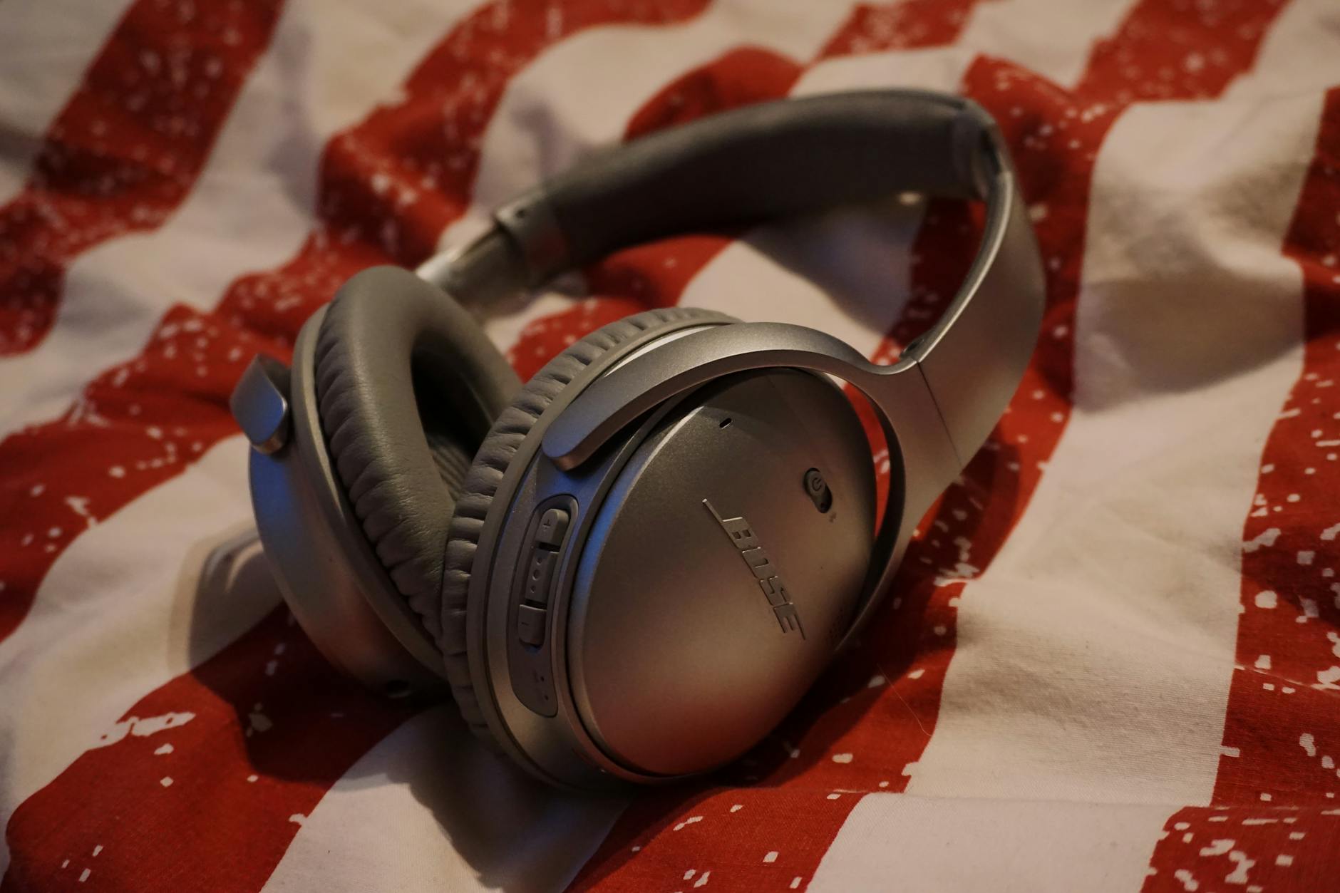 Close-up of silver wireless headphones resting on red and white patterned fabric.